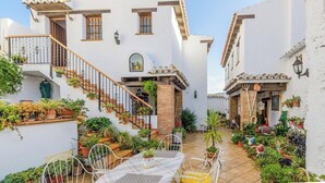 A courtyard with a dining table and chairs, surrounded by potted plants and a staircase leading to a building. - Las Monjas - Atroe Periana by Ruralidays (Málaga)