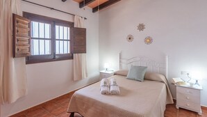 Une chambre à coucher comprenant un lit, deux tables de chevet, une fenêtre avec des volets et un élément décoratif mural.