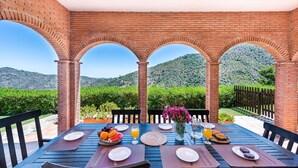 A table set for breakfast with a view of a vineyard and hills.