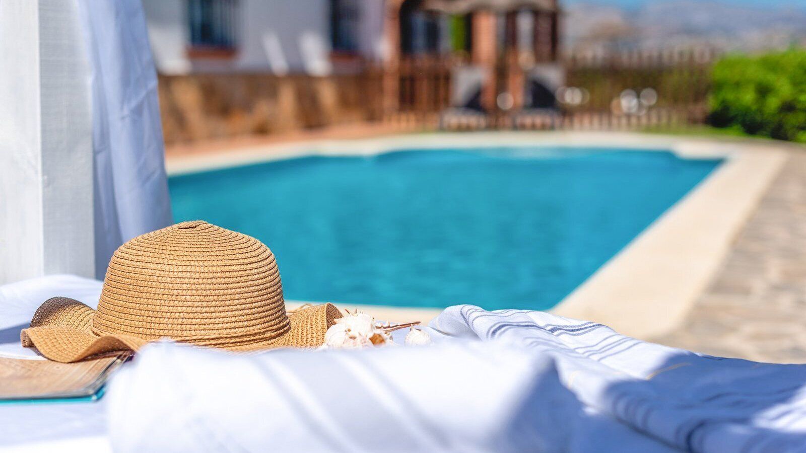 Una tumbona con un sombrero de paja y conchas marinas junto a una piscina.