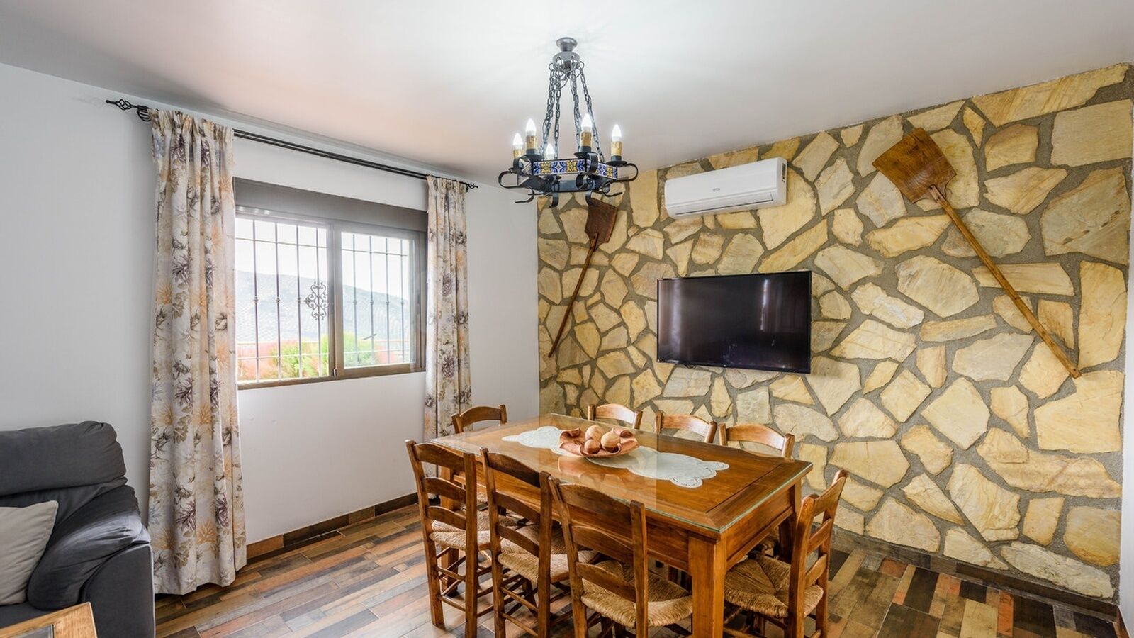 Un comedor con pared de piedra, televisión de pantalla plana y candelabro.