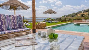 A poolside area with a lounge chair, a table with a teapot, cups, and apples, and a view of the pool and surrounding landscape. - Villa Fraskito Iznájar by Ruralidays (Córdoba)