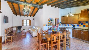 A spacious living area with a fireplace, a dining table with chairs, a sofa, and a kitchen with wooden cabinets and a tiled backsplash.