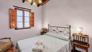 A bedroom with a bed, two bedside tables with lamps, a wooden chair, and a window with wooden shutters.