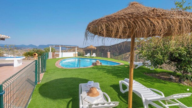 A pool area with a thatched umbrella, white lounge chairs, and a view of the mountains.