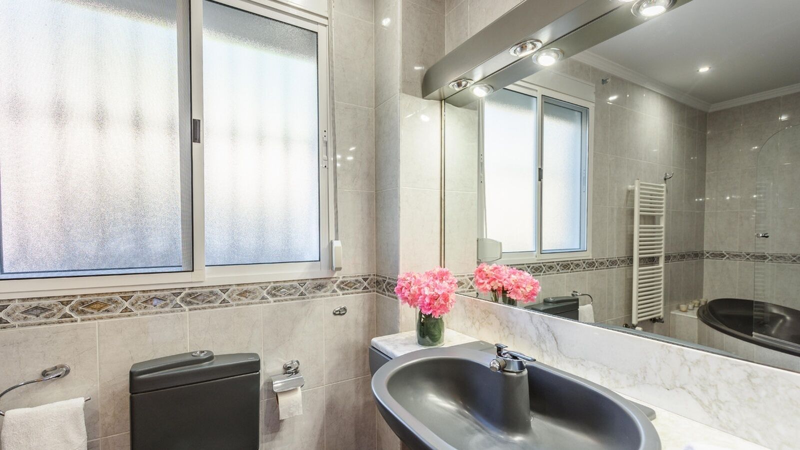 A modern bathroom with a large mirror, a bathtub, and a sink.