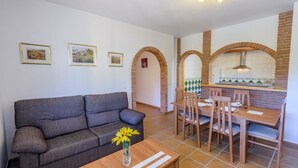 Un salon avec un canapé, une table à manger avec des chaises et un coin cuisine agrémenté d’une arche en briques.