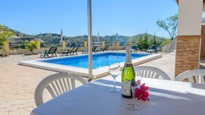 Une table au bord de la piscine, avec une bouteille de vin, deux verres et une fleur.