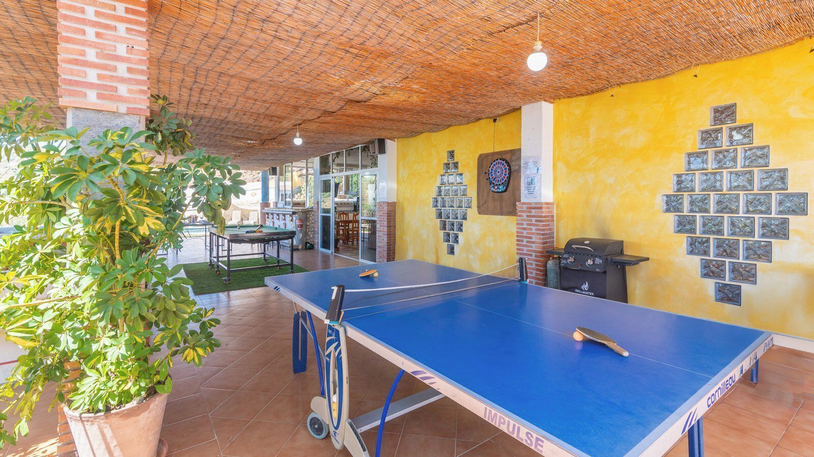 A ping pong table in a room with yellow walls, a brick column, and a plant.