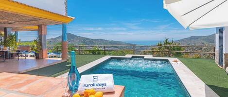 A pool area with a view of hills, a table with a towel, and a bottle.