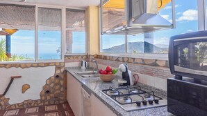 A kitchen with a stone wall, a gas stove, a sink, and a window overlooking a scenic view. - Cortijo La Encina Sayalonga by Ruralidays (Málaga)