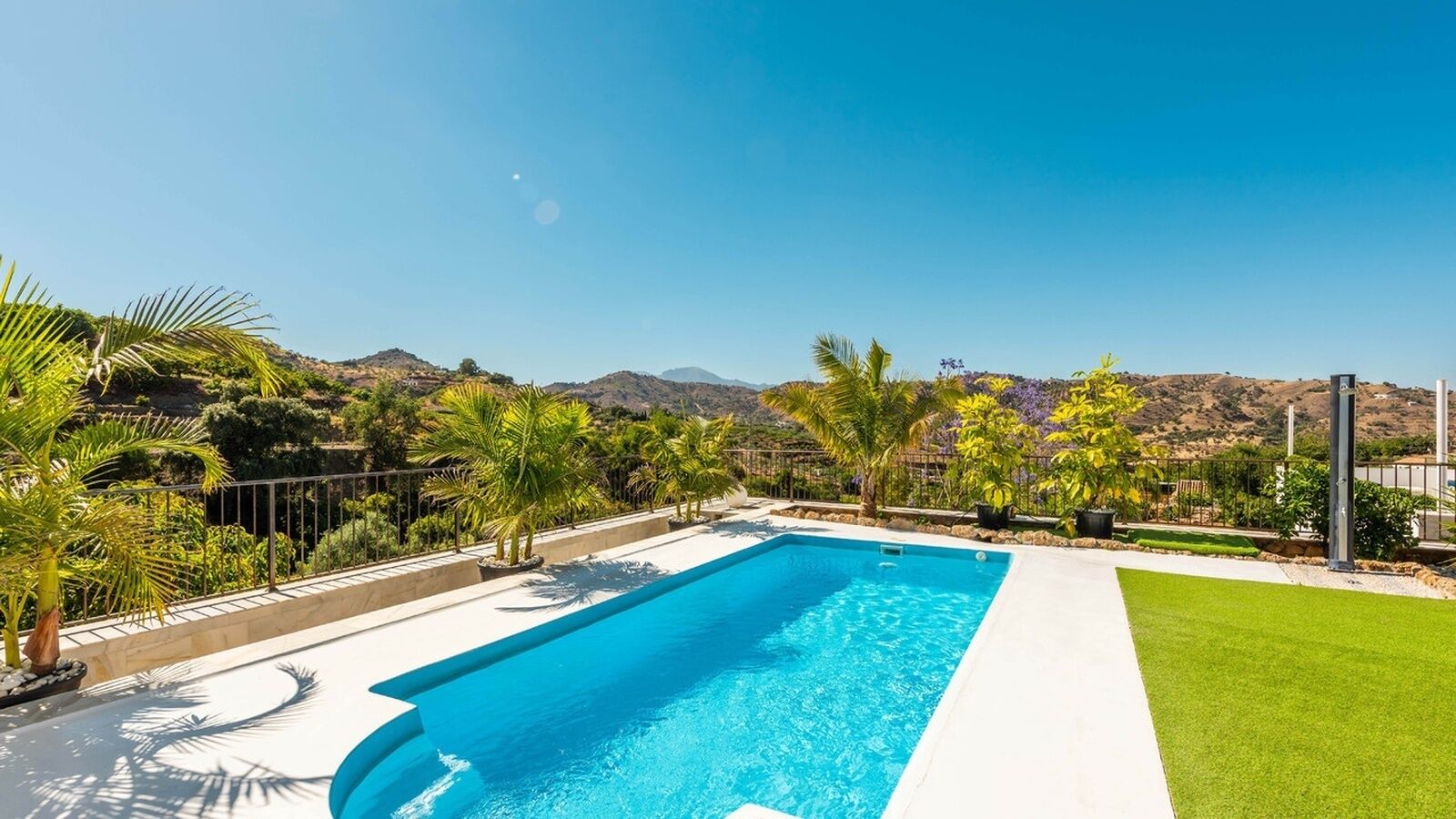 A rectangular swimming pool with clear blue water, surrounded by a white deck and a green lawn.