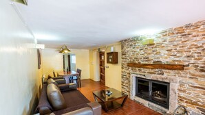 A living room with a stone fireplace, a sofa set, a dining table, and a kitchen area in the background. - Los Albardinales -  Casa Blanqueta Tabernas by Ruralidays (Almería)
