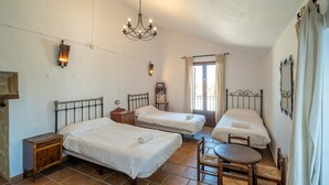 Une chambre avec trois lits, un lustre, une petite table et une fenêtre avec des rideaux.