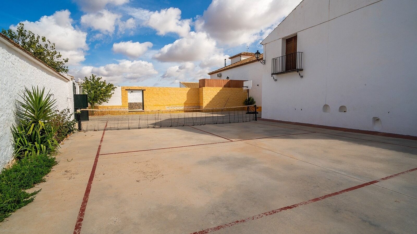 Une cour avec un terrain de basket, un bâtiment blanc doté d’un balcon et un bâtiment jaune avec une porte.
