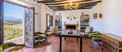 A room with a fireplace, a dining table, and chairs. There is a view through a glass door.