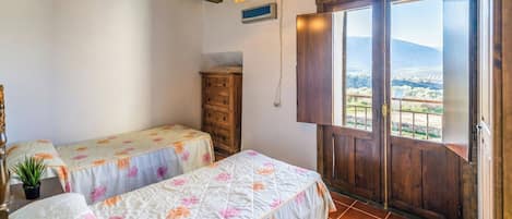 A bedroom with two beds, a wooden dresser, a potted plant, and a balcony with a view.