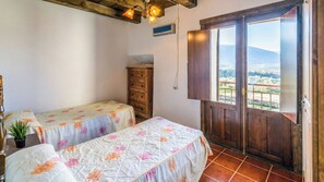 A bedroom with two beds, a wooden dresser, a potted plant, and a balcony with a view. - Cortijo Vaquero Rural Loja by Ruralidays (Granada)