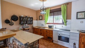 Une cuisine avec des meubles en bois, un plan de travail en pierre, un évier, une cuisinière et une fenêtre ornée de rideaux verts.