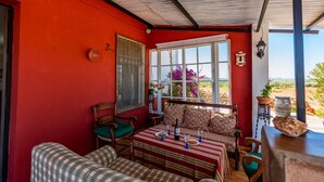 Une pièce chaleureuse avec un mur rouge, un banc en bois, une table recouverte d’une nappe à rayures et une vue sur l’extérieur.