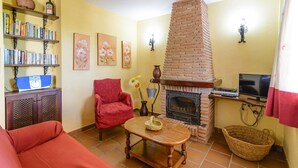 A living room with a fireplace, a red armchair, a bookshelf, and a television. - Cortijo Los Tulipanes Periana by Ruralidays (Málaga)