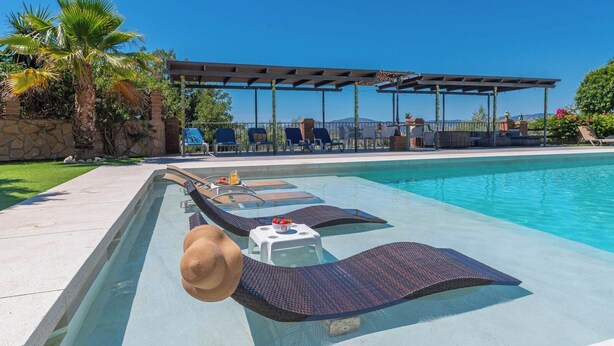 A poolside area with lounge chairs, a small table with a drink, and a pergola with string lights. - Cortijo Los Tulipanes Periana by Ruralidays (Málaga)