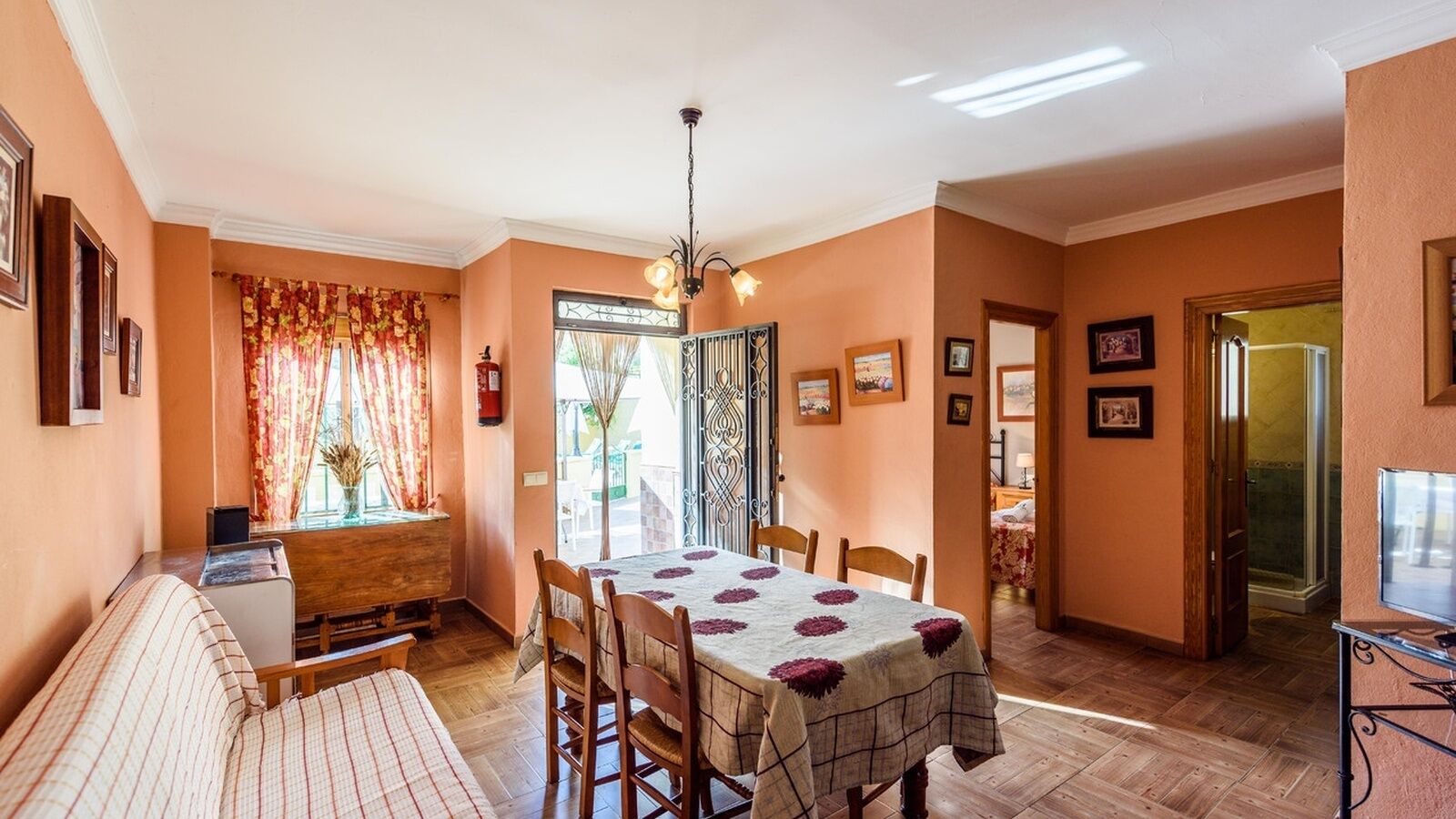 A cozy dining area with a wooden table, chairs, and a bench. A window with curtains and a door leading outside are visible.