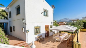Ein weißes Gebäude mit einer Terrasse, Sitzgelegenheiten im Freien und Blick auf die Berge.