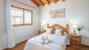 A bedroom with a wooden headboard, a large bed with white bedding, two bedside tables with lamps, and a painting on the wall. - Balcon de la Axarquia Almáchar by Ruralidays (Málaga)
