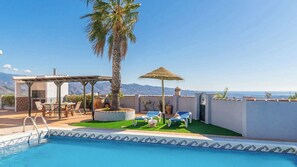 A pool area with a pergola, lounge chairs, and a palm tree.