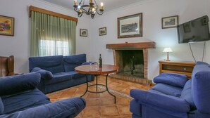 A living room with blue sofas, a round wooden table, a fireplace, and a television mounted on the wall.