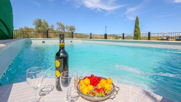 A poolside table with a bottle, glasses, and a bowl of fruit.