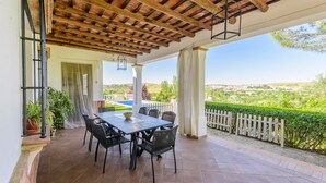 A covered patio with a table and chairs, a view of the countryside, and a wooden ceiling.