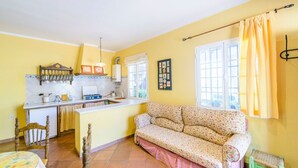 A compact kitchen with a dining area, a sofa, and a window with curtains.