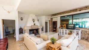 A spacious living room with a fireplace, white sofas, a TV, and stone accents. - Cortijo La Vega Archidona by Ruralidays (Málaga)