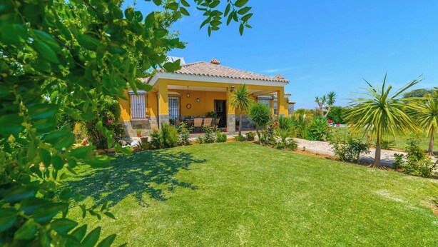 A yellow building with a tiled roof, surrounded by a well-maintained lawn and various plants. - Casa Quintero 4 dorm Conil de la Frontera by Ruralidays (Cádiz)