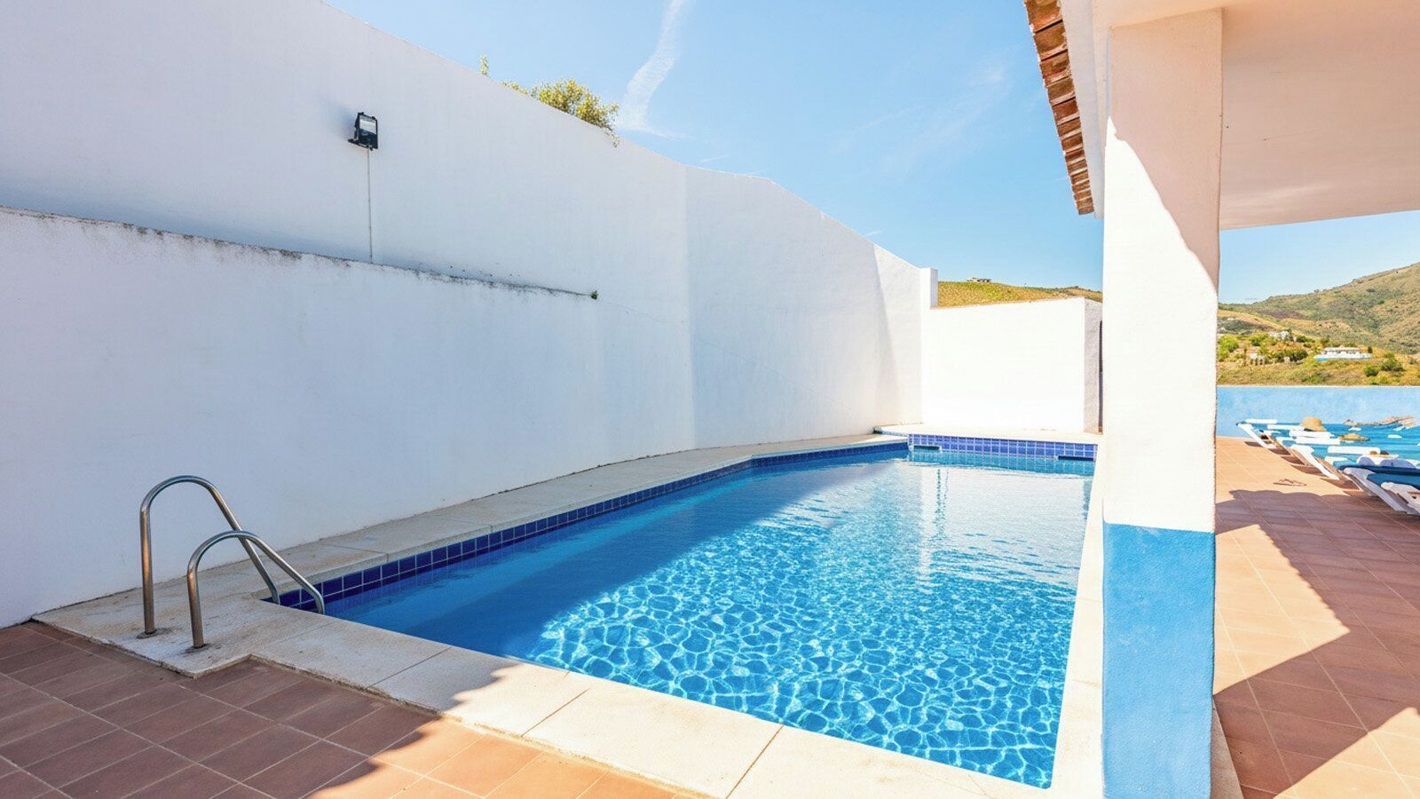 A swimming pool with a metal ladder, tiled edges, and a clear blue water surface.