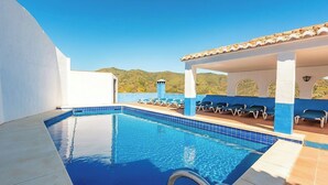 A clear blue pool with lounge chairs and a covered area, surrounded by white walls and a view of green hills. - Alejandro de Almachar Almáchar by Ruralidays (Málaga)