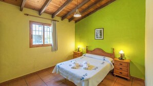 A bedroom with a wooden ceiling, a bed with a floral bedspread, two bedside tables with lamps, a window with curtains, and a green wall. - Alejandro de Almachar Almáchar by Ruralidays (Málaga)