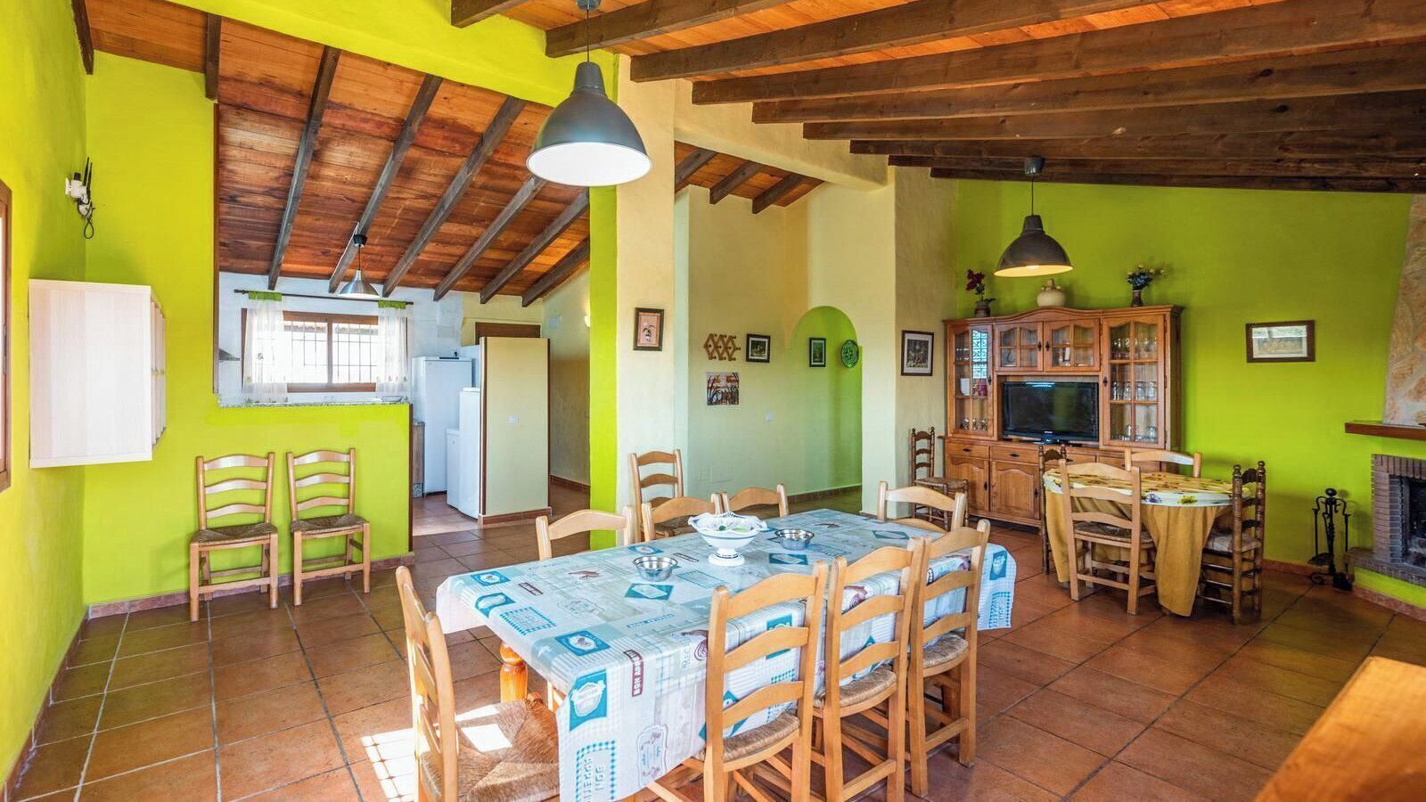 A dining area with a wooden table and chairs, a kitchen in the background, and a fireplace.