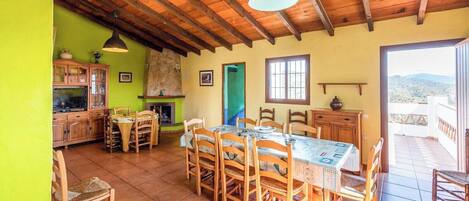 A dining area with a large table and chairs, a kitchen with cabinets and a stove, and a view of the outdoors through a door.