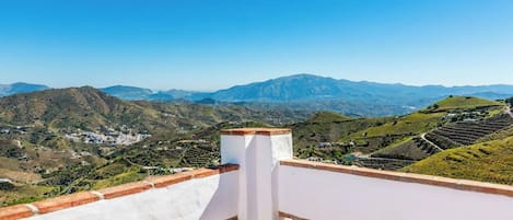Une terrasse dotée d’une balustrade blanche, qui offre une vue sur un paysage montagneux parsemé de vignobles en terrasses.