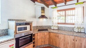 A compact kitchen with granite countertops, a built-in microwave, a stove, and wooden cabinets. - Alejandro de Almachar Almáchar by Ruralidays (Málaga)