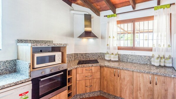 A compact kitchen with granite countertops, a built-in microwave, a stove, and wooden cabinets. - Alejandro de Almachar Almáchar by Ruralidays (Málaga)