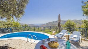Ein Poolbereich mit freiem Blick auf die Landschaft, ein Tisch mit Snacks und Getränken sowie Liegestühle.