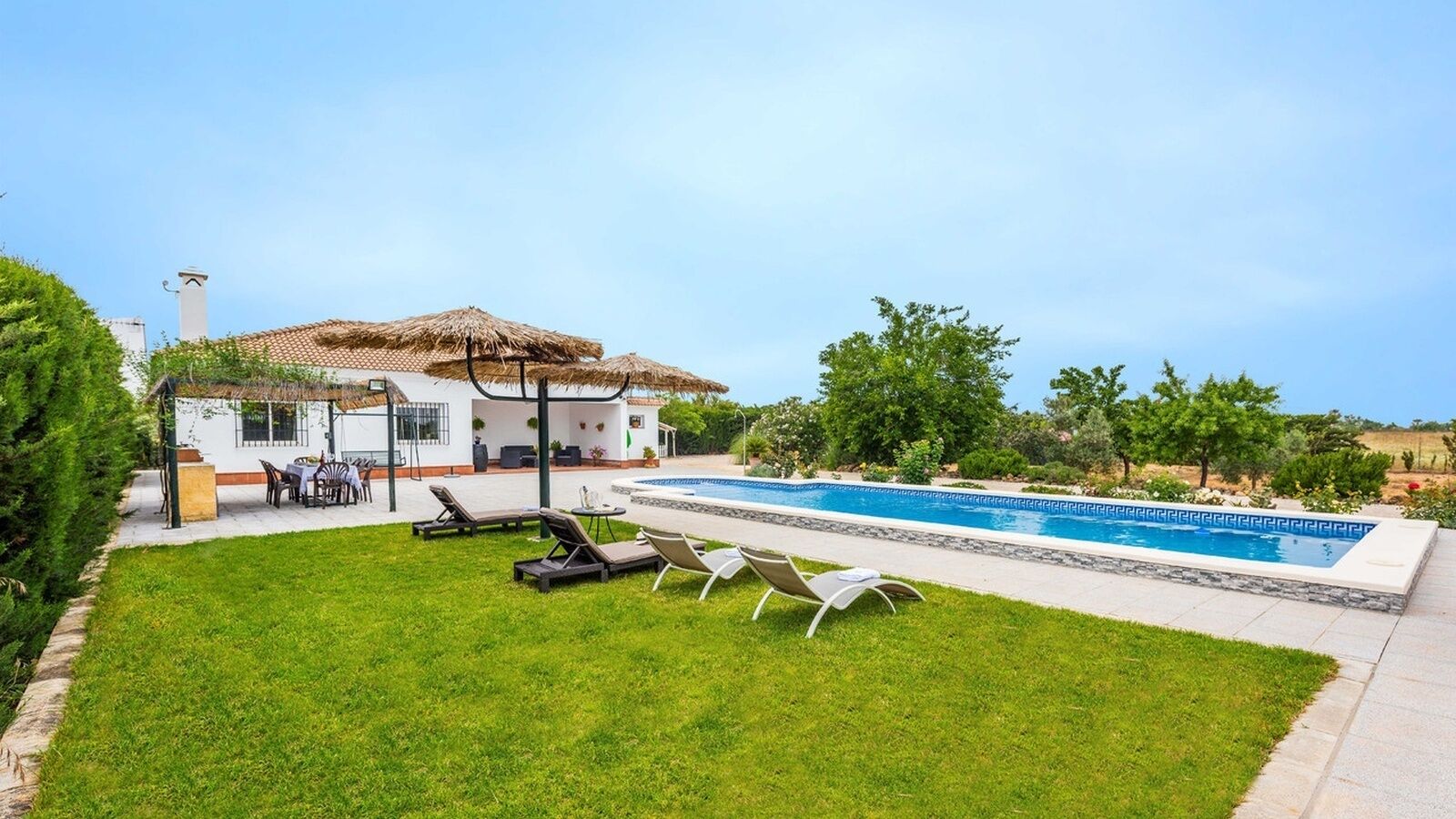 Una casa con piscina, un patio con poltrone relax e un giardino.