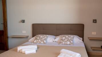 A neatly made bed with a brown headboard, two pillows with a floral pattern, and rolled towels on the bed.