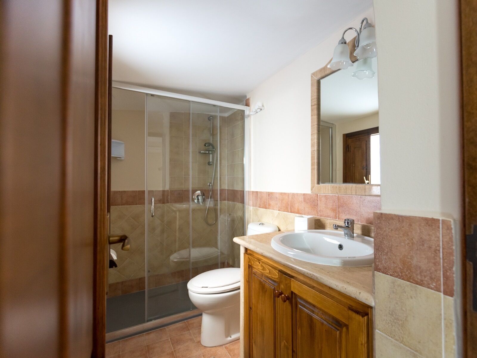 A bathroom with a glass-enclosed shower, a toilet, a sink, and wooden cabinets.