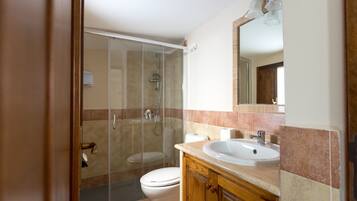 A bathroom with a glass-enclosed shower, a toilet, a sink, and wooden cabinets.