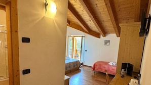 A cozy room with wooden beams, a bed, a small table with a kettle, and a door with a light switch. - Agriturismo Girardelli (Riva del Garda)